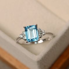 a ring with an aqua blue topaz surrounded by white diamonds in a gift box