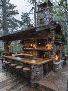 an outdoor bar in the woods with stools around it and lights hanging from the roof