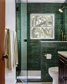 a green tiled bathroom with a toilet, sink and shower in front of a window