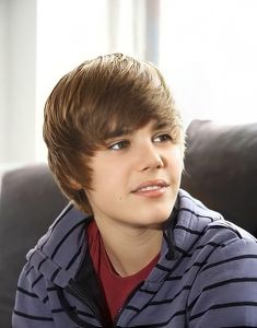 a young boy sitting on top of a black couch next to a window and wearing a striped shirt