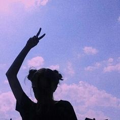 a woman is holding her hand up in the air while she stands under a cloudy blue sky