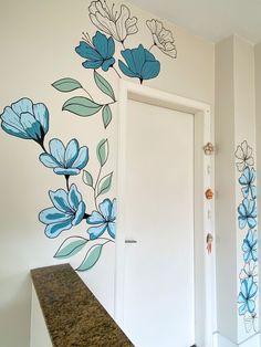 a white door sitting next to a wall with blue flowers painted on it's side