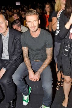 a man sitting next to another man in front of a crowd at a fashion show