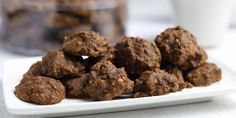 a white plate topped with chocolate truffles next to a glass of milk and a container of cookies