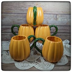 four yellow ceramic pumpkin mugs sitting on top of a doily