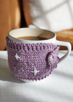 a coffee cup with a crocheted handle is sitting on a table next to a pillow