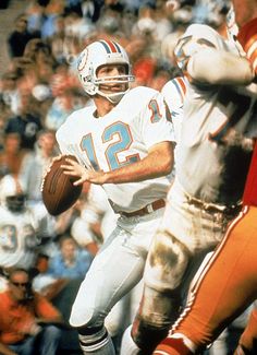 a football player is holding the ball in his hand and running with the other team behind him