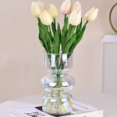 a vase filled with white tulips sitting on top of a table next to a book