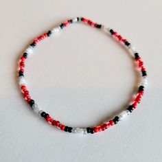 a red, white and black beaded necklace on a white surface with space for text