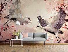 two birds flying over a couch in front of a wall with pink flowers on it