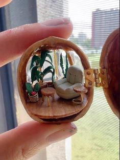 someone is holding a miniature living room in their hand, with plants and furniture visible through the glass