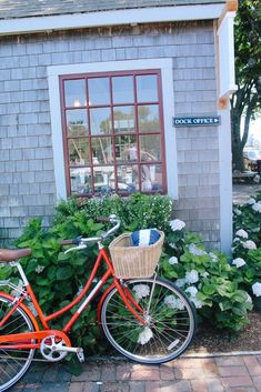 an orange bicycle parked in front of a building with flowers and shrubs around it on the sidewalk