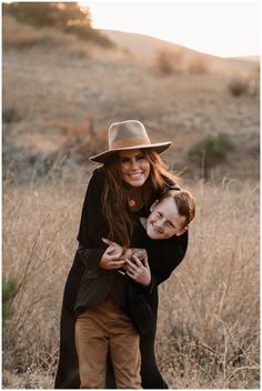 a woman holding a boy in her arms while standing in the middle of a field