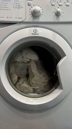 a washing machine with the front door open and dirty clothes in it's washer