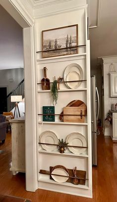 a white book shelf filled with lots of plates and other items on top of a hard wood floor