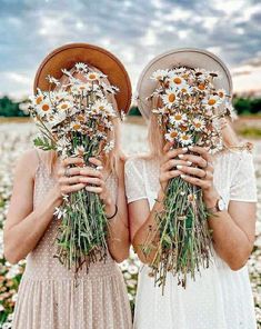 two women standing in a field with daisies and holding their hands up to their faces