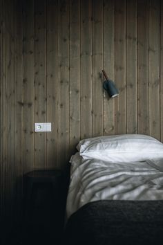 a bed with white sheets and pillows in a room that has wood paneling on the walls