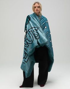 a woman standing in front of a white background wearing a blue and black shawl