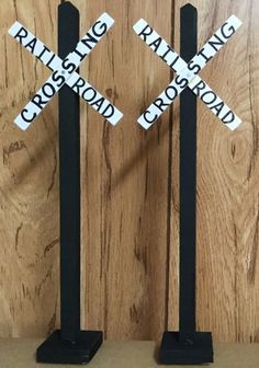 two black and white railroad crossing signs sitting on top of a wooden table next to each other