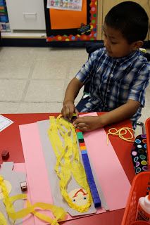 a young boy sitting at a table working on some crafting material with scissors and tape