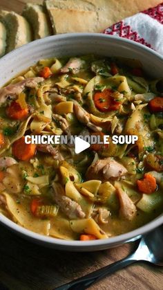 a bowl of chicken noodle soup with bread in the background