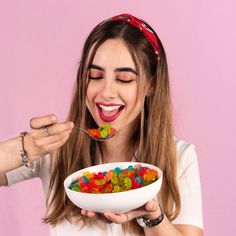 a woman eating gummy bears out of a white bowl with a spoon in her hand