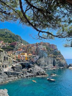 boats are in the water next to a rocky shore with houses and cliffs on it