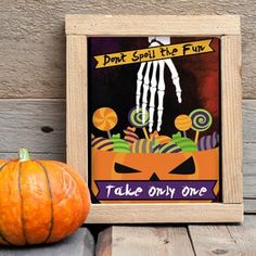 an orange pumpkin sitting next to a wooden frame with a handprinted skeleton on it