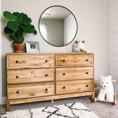 a white teddy bear sitting on top of a wooden dresser next to a round mirror