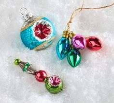 three ornaments are laying on the snow and one is hanging from a string with bells