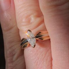 a person's hand holding a ring with a diamond on it and the middle finger