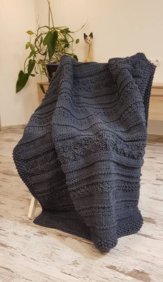 a knitted blanket sitting on top of a wooden floor next to a potted plant