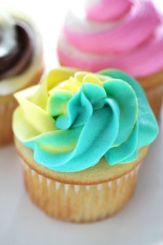 three cupcakes with different colored frosting on them sitting on a white plate