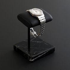 a watch sitting on top of a black marble block with a metal bracelet around it