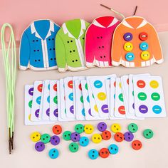 several different colored buttons and pins next to some knitting needles on a white surface with pink background