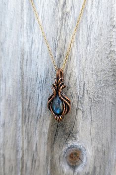 a gold necklace with a blue stone in the center on a wooden surface, next to a piece of wood