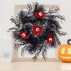 a halloween wreath with red roses and black feathers is displayed in front of a pumpkin