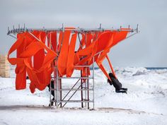 an orange sculpture is in the middle of snow covered ground with two people standing underneath it