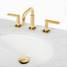 a bathroom sink with two gold faucets and a white marble countertop top