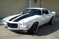 a white and black striped muscle car parked in front of a garage with two doors