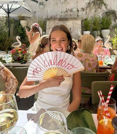 a woman sitting at a table holding a fan