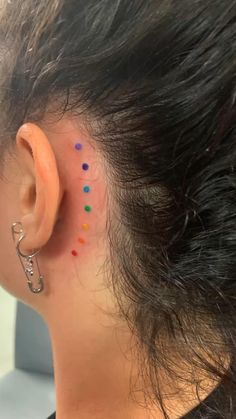 a woman's left ear with colorful dots on the back of her head and behind her ear is a pair of scissors