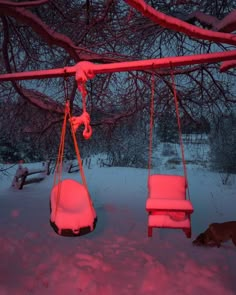 a swing and chair covered in snow under a tree at night with red lights on it