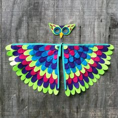 a colorful bird made out of paper sitting on top of a wooden fence next to a pair of scissors