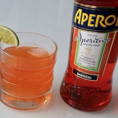 a bottle of aperoli next to a glass filled with orange juice and lime