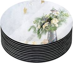 a stack of black and white plates sitting on top of a table with flowers in it