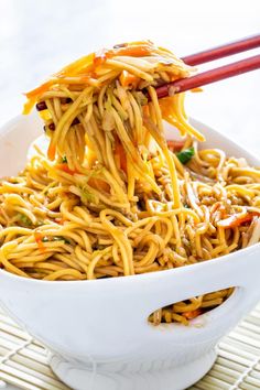 noodles being lifted with chopsticks in a white bowl on top of a table