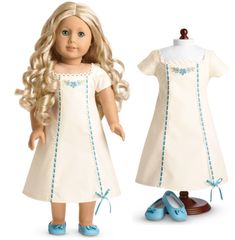 the doll is wearing a white dress with blue trims on it and shoes are next to her