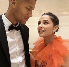 a man in a tuxedo standing next to a woman wearing an orange dress