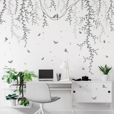 a white desk topped with a laptop computer next to a wall covered in birds and branches